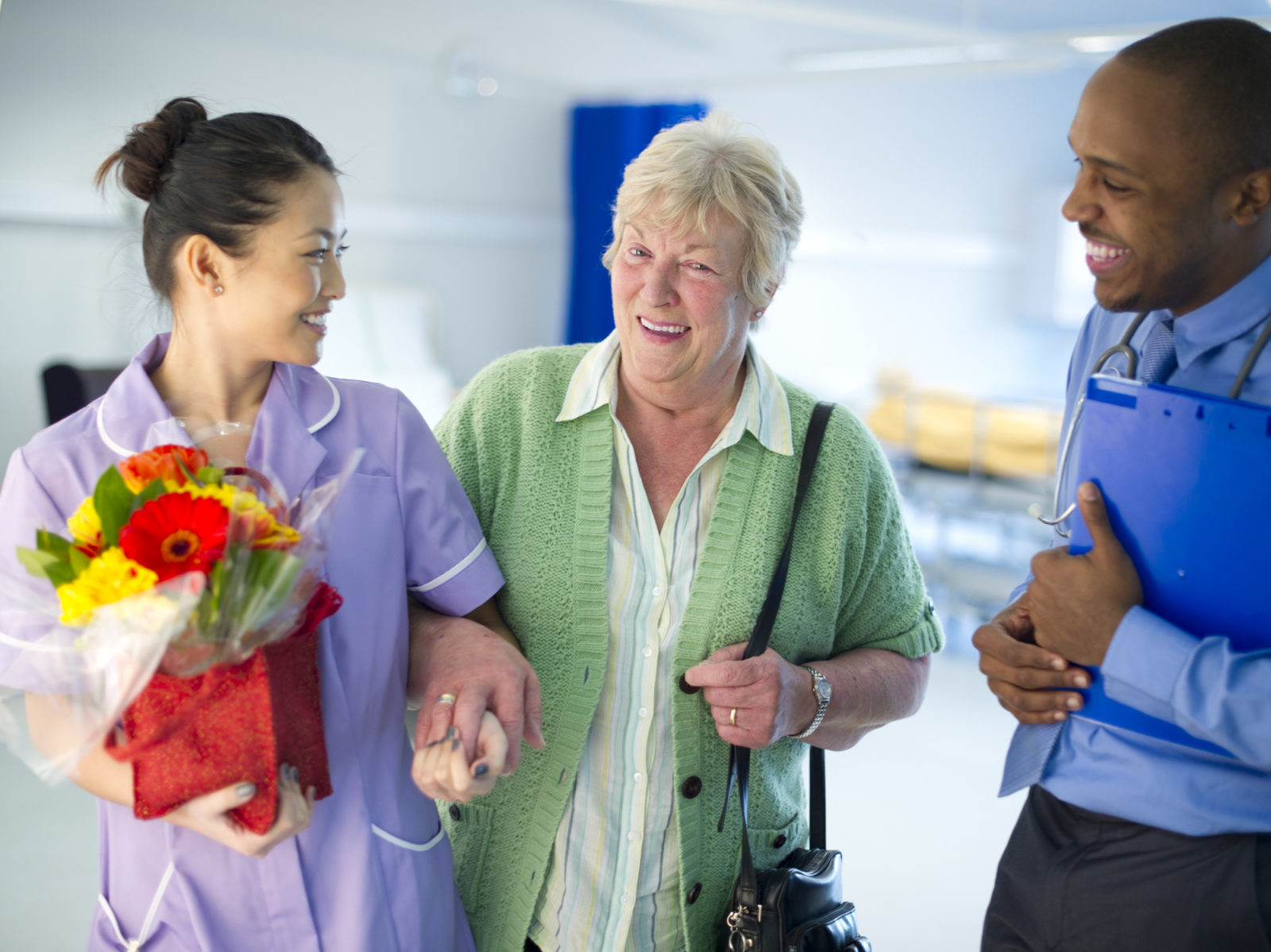 elder woman leaving hospital with aid of doctor and nurse