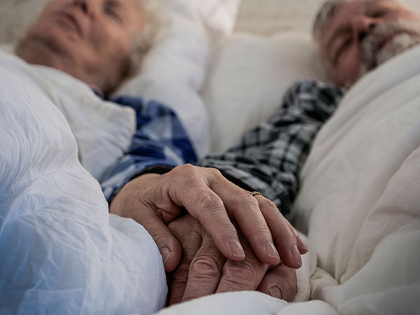 Close up of hands holding of senior couple in bed